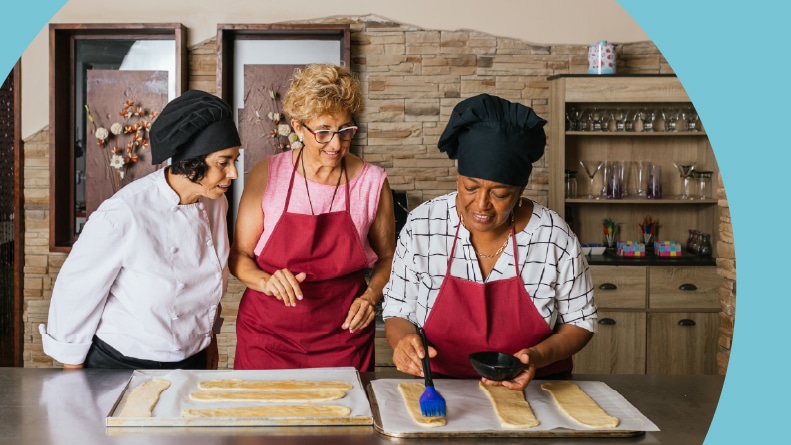 A chef guiding students while brushing pastry in a baking class.