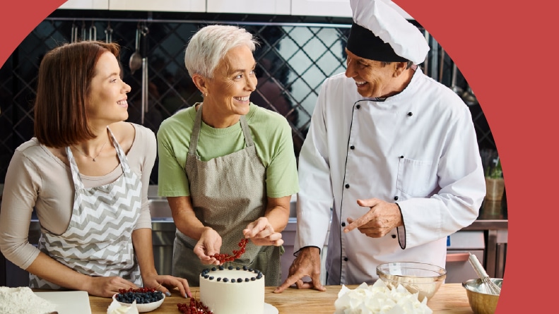 55+ women smiling at a chef in a cake decorating class.