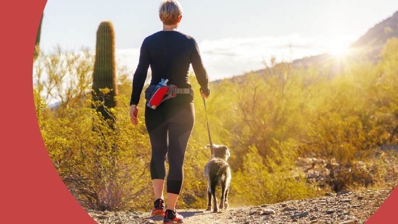 A 55+ woman walking a dog on a hiking path in Mountain View Park in Phoenix, Arizona.