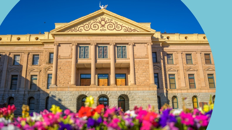 Arizona State Capitol in Phoenix, AZ, with colorful flowers in the foreground under a blue sky.