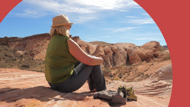 An active 55+ woman in a hat sitting in Red Rock and admiring the views of the canyon.