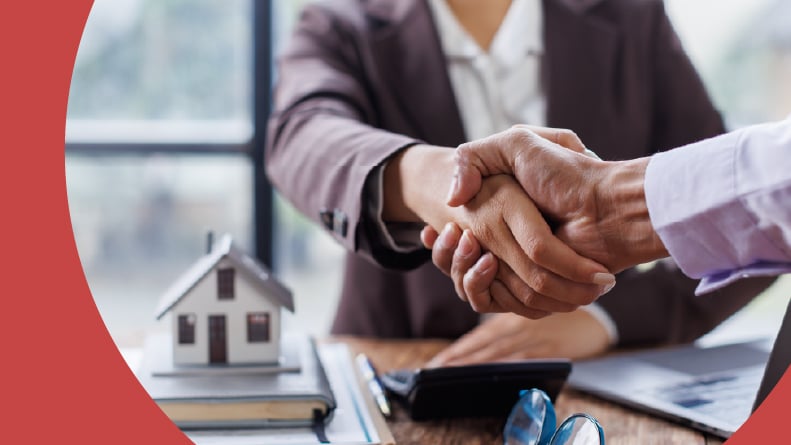 A real estate agent shaking hands with a client and making home sale documents.