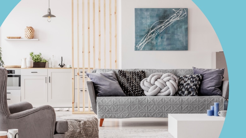 Open plan condo with a small, white kitchen and a living room with grey couch and a wooden coffee table.