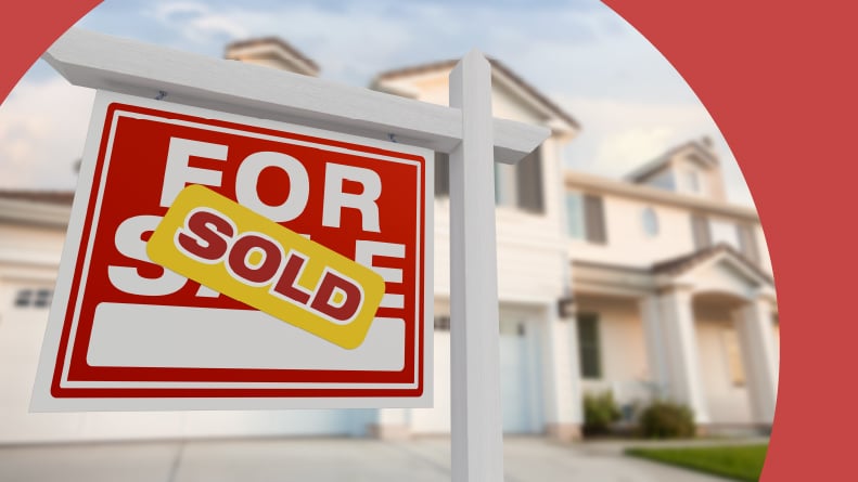 A "sold" sticker on a "for sale" sign in front of a house.