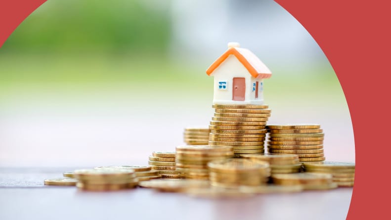 A mini house model on a stack of gold coins.