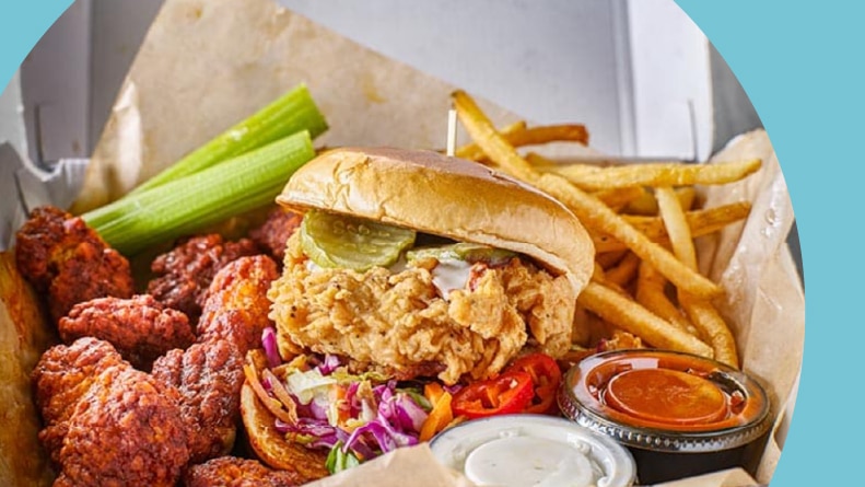 A take out box with a fried chicken sandwich, boneless wings, and french fries.
