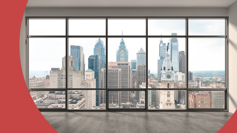 An empty room with a view out the window of the Downtown Philadelphia skyline.