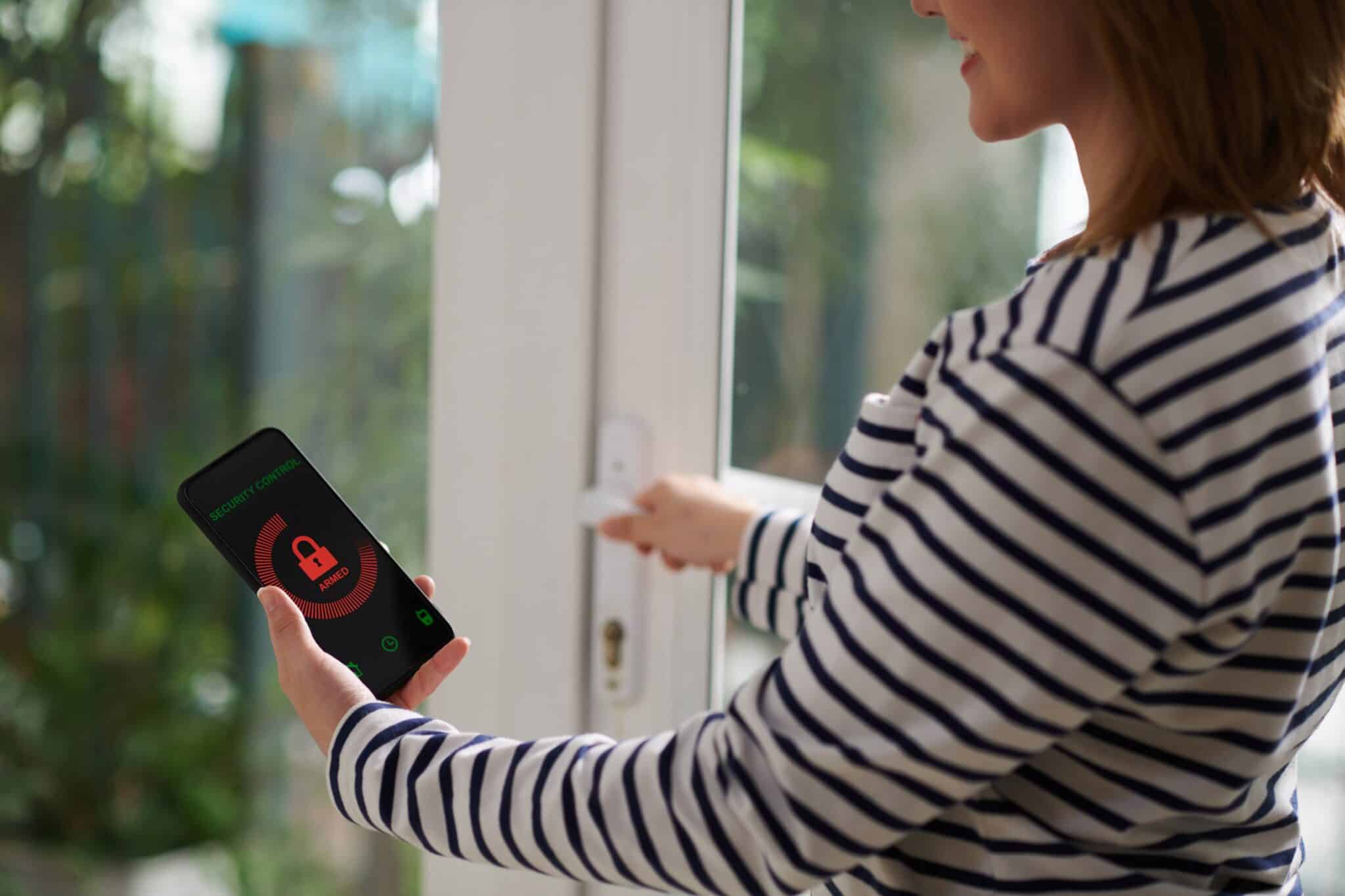 A smiling woman setting a home security system with a mobile app.