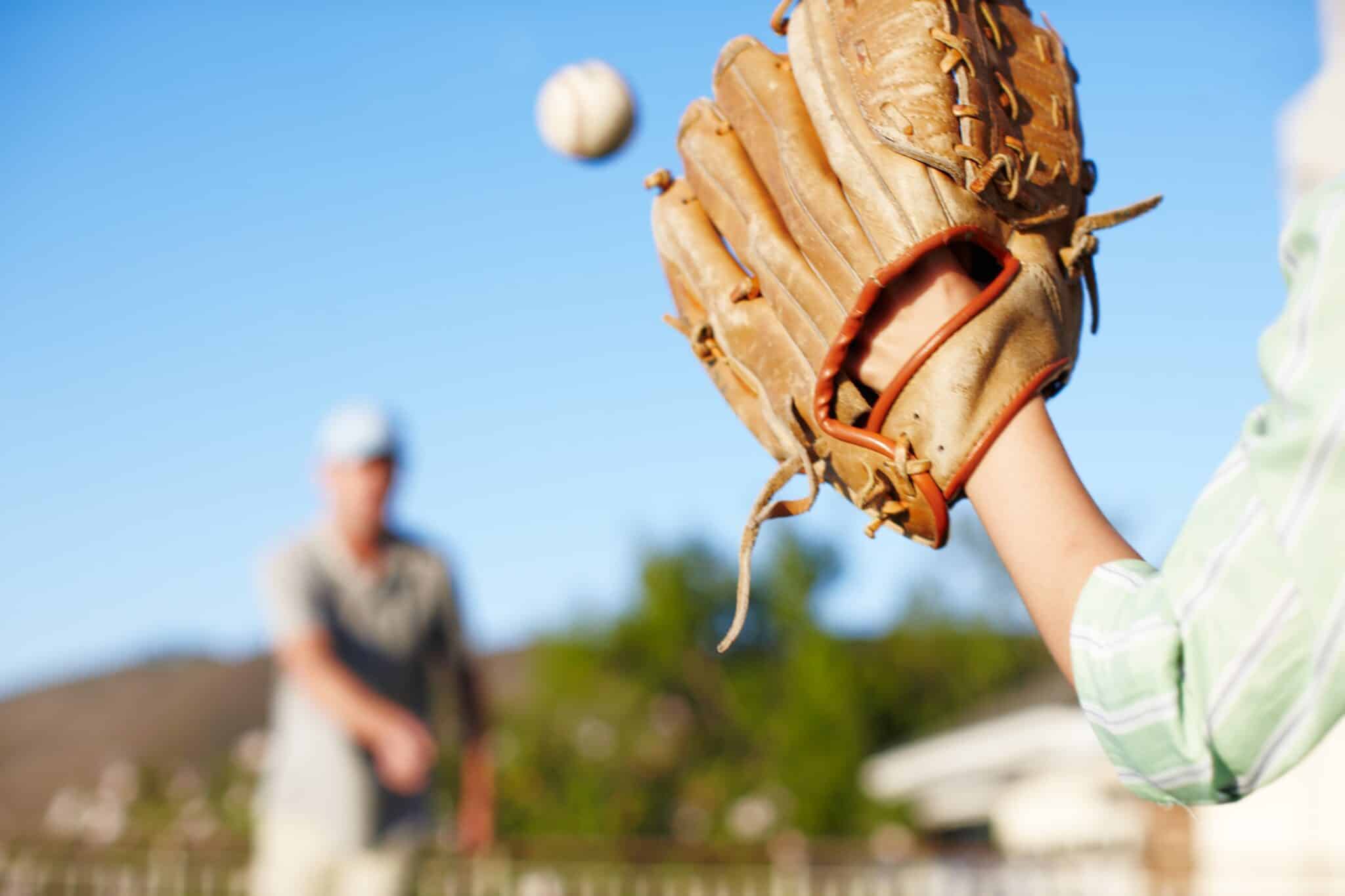 Two 55+ adults playing catch with a softball and softball gloves.