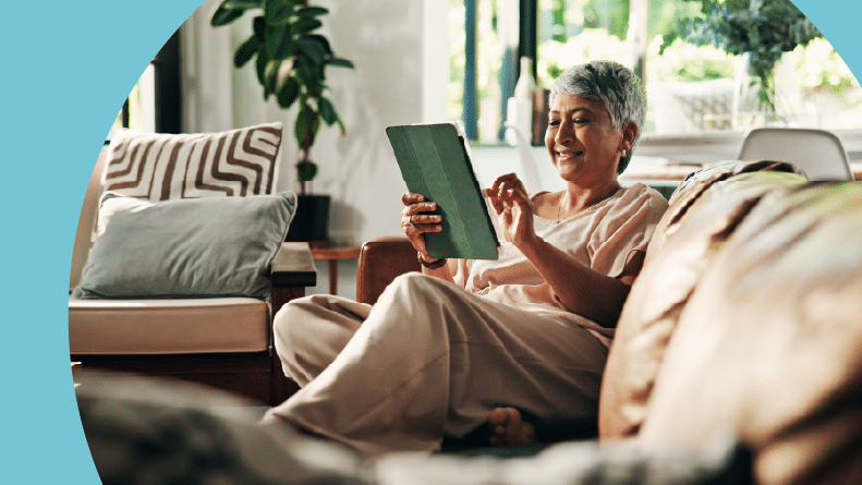 A 55+ woman browsing home listings on her tablet while sitting on a couch.