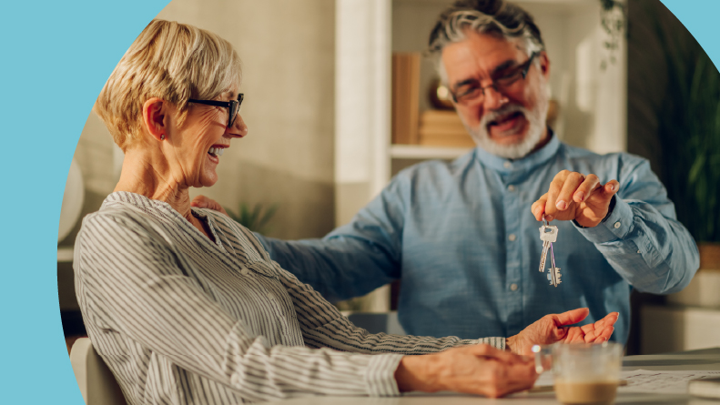 A happy 55+ couple sitting at a table and holding their new house keys.