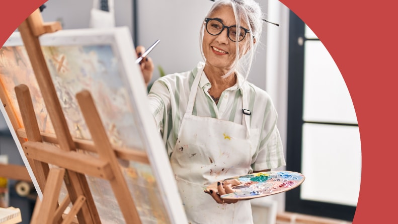 A retired woman smiling and painting in an art studio in her 55+ community.
