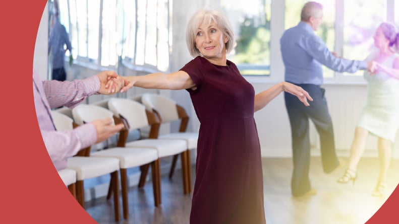 A smiling 55+ woman in elegant clothes learning to dance in a couples jazz dance class.