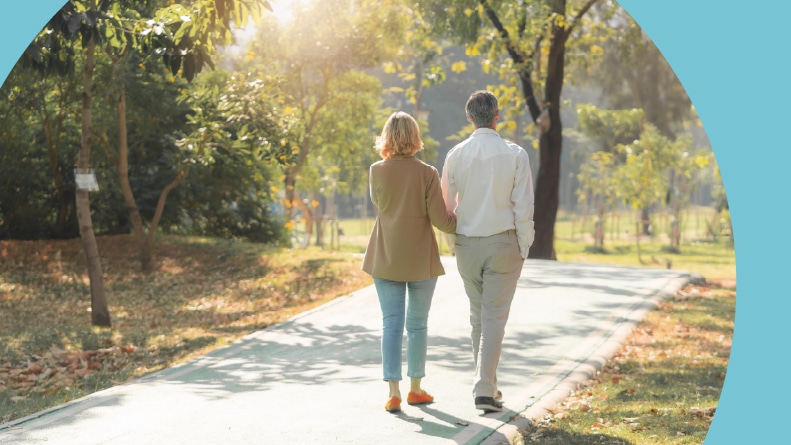 A 55+ couple walking through a park.