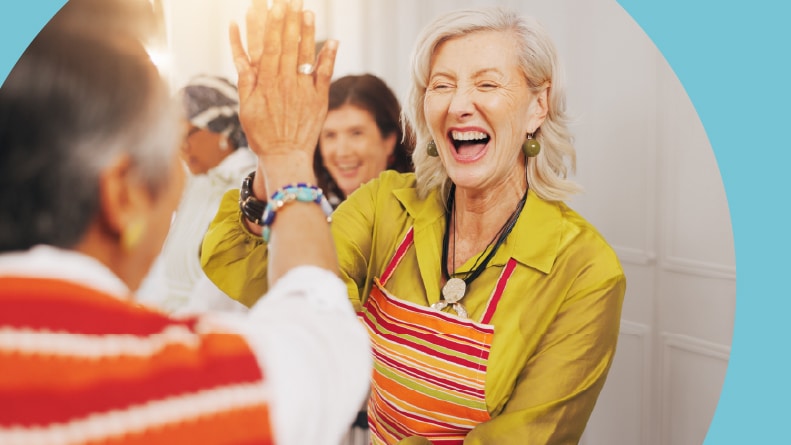 Two 55+ friends high five in a cooking class in their community.