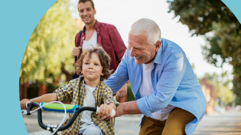 A father and grandfather teaching a young boy to ride a bike on a residential street.