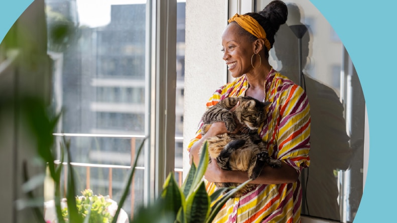 A smiling 55+ woman with her cat in her apartment.