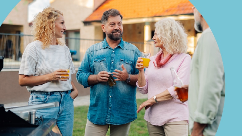 Four friends enjoying drinks and engaging in lively conversation in a backyard in a 55+ community.