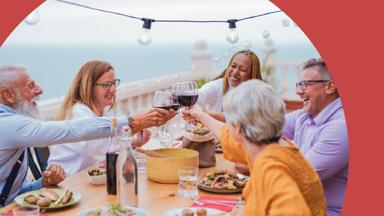 A group of 55+ friends toasting with wine while enjoying dinner on the balcony of a villa.