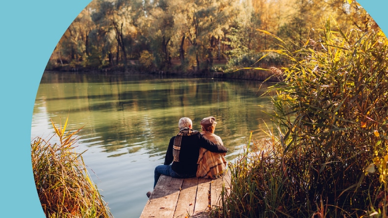 A 55+ couple relaxing by a lake in autumn.