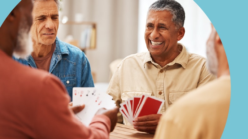 A group of 55+ men playing card games on a wooden table.