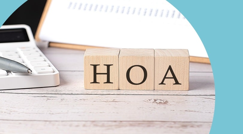 Wooden letter blocks spelling HOA on a white wood desk beside a calculator, pen, and clipboard of figures.