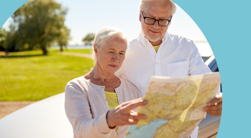 Senior couple standing beside their car reading a road map on a sunny day.