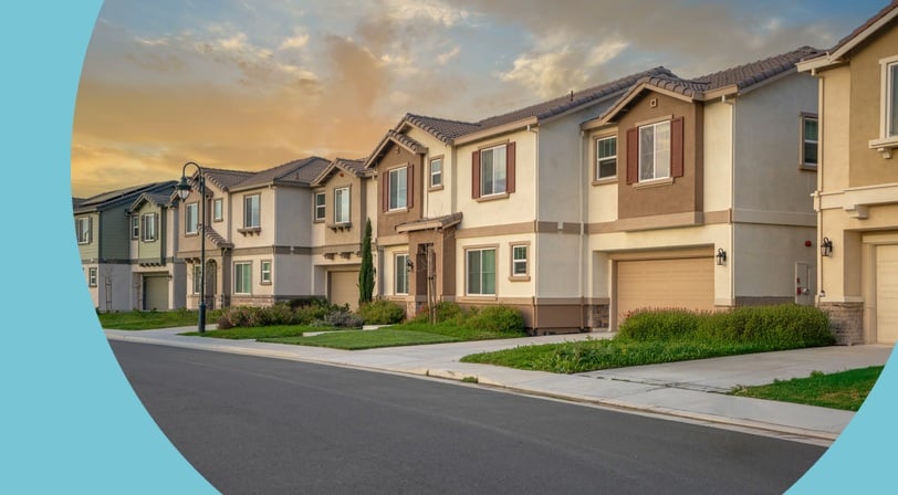 A quiet residential street lined with two-story homes and manicured front lawns at sunset.