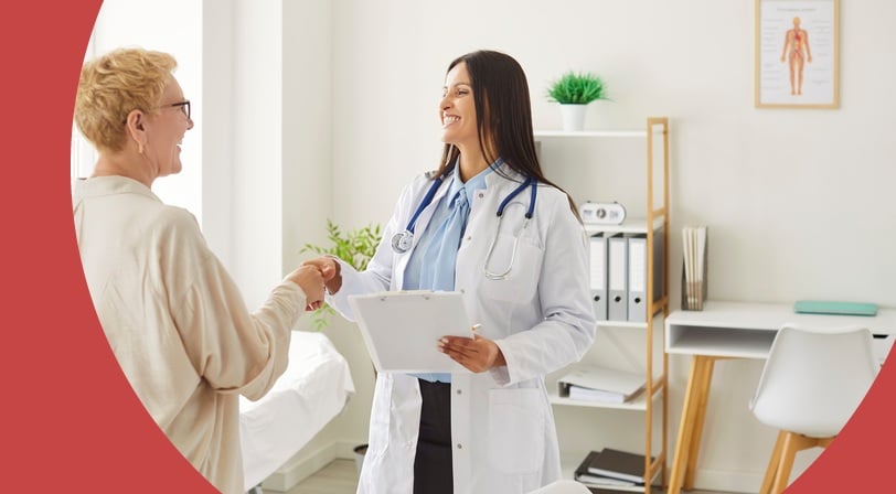 Smiling doctor shaking hands with an older woman in a medical office.