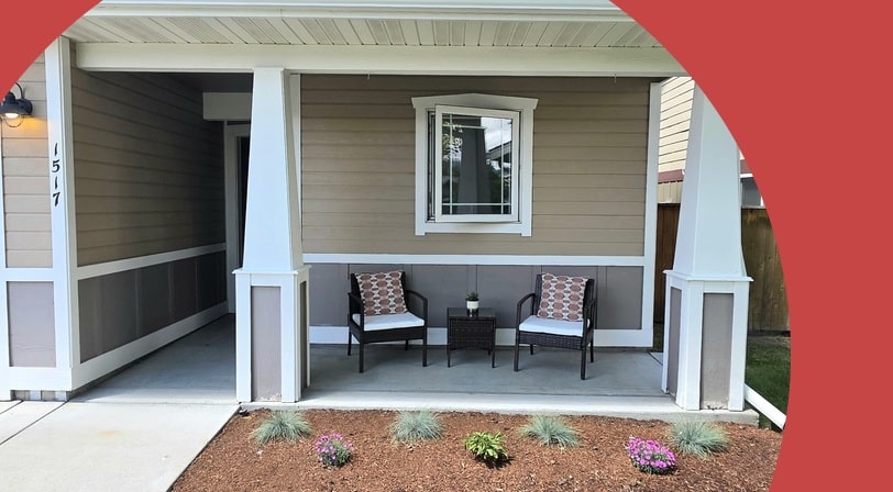 Covered front porch of a single-story home with two cushioned patio chairs and a low-maintenance flower bed.