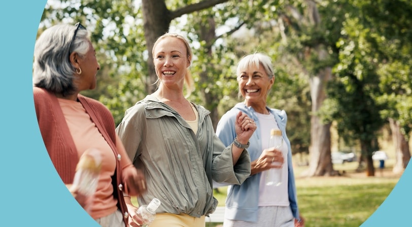 Three women laughing together while walking through a tree-filled park.