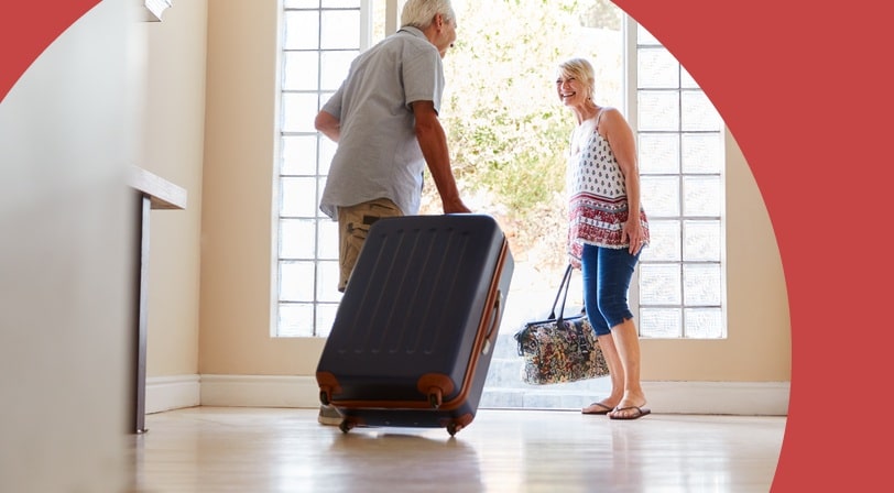 Senior couple arriving home with a rolling suitcase and travel bag.