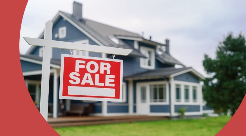 A red "For Sale" sign stands in the front yard of a blue two-story house with white trim and a covered porch.