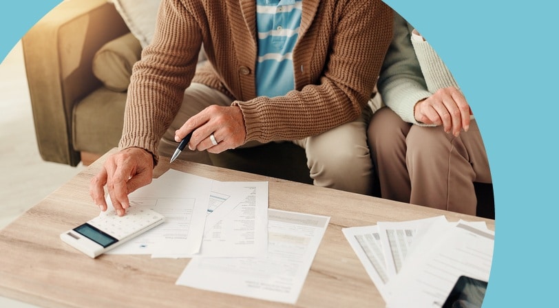A 55+ couple reviewing financial documents with a calculator at a coffee table.