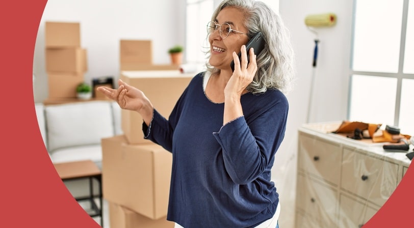 Woman with gray hair talking on her phone surrounded by moving boxes.