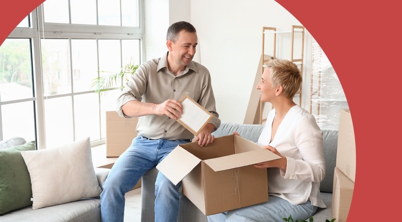 A mature couple unpacking a cardboard box together in their new living room.
