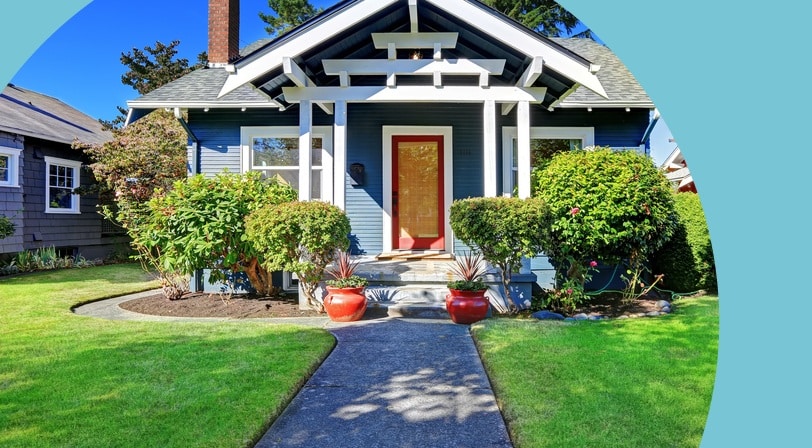 Charming blue craftsman-style home with a red front door, manicured shrubs, and a welcoming front walkway, typical of homes found in many 55+ communities.