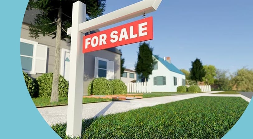A "For Sale" sign on the lawn in front of a house.