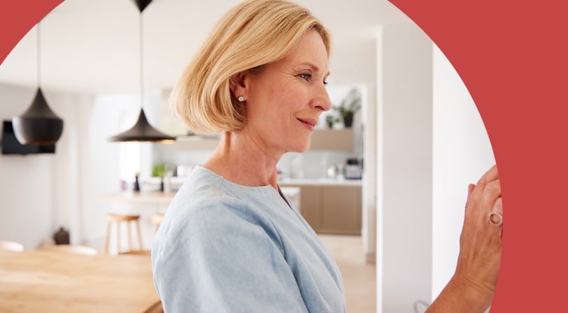 A 55+ woman adjusting a wall-mounted thermostat in a bright, modern kitchen.