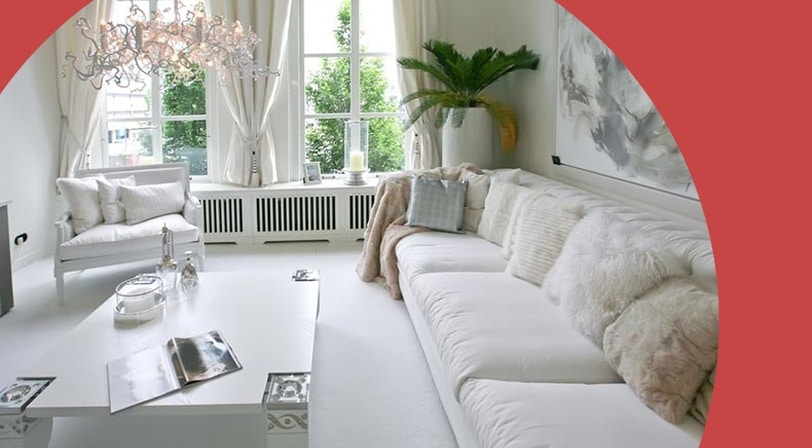 A bright white living room with a long sofa, plush pillows, and arched windows.
