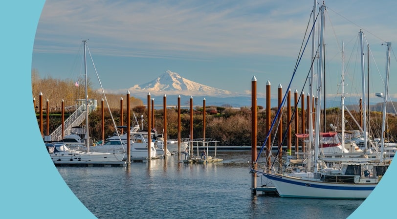 Sailboats docked at Tidewater Cove marina in Vancouver, Washington with a snowy mountain peak visible in the distance.