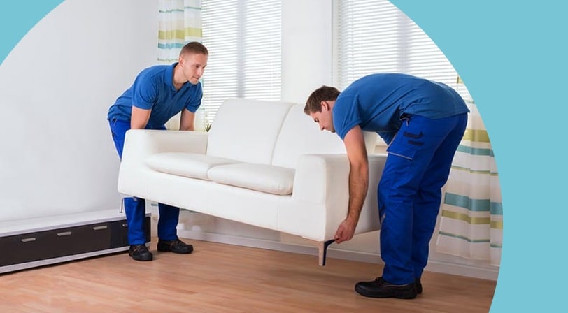 Two professional movers carrying a white loveseat into a living room.