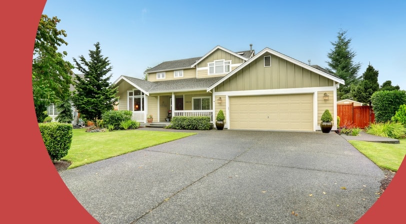 A tan two-story house with a covered front porch, attached garage, and a long driveway bordered by manicured landscaping.