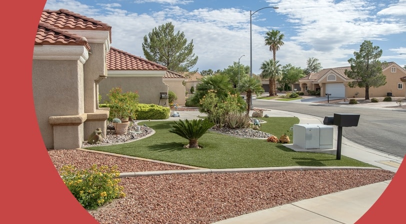 A single-story home with a red tile roof and desert landscaping, featuring artificial turf, a small palm tree, and gravel beds along the front yard.