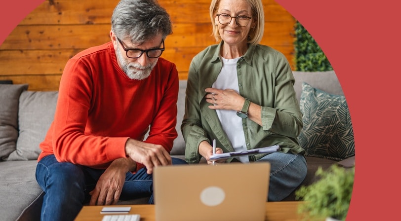 A mature couple reviews 55+ communities together on a laptop, with a calculator and credit card on the coffee table in front of them.