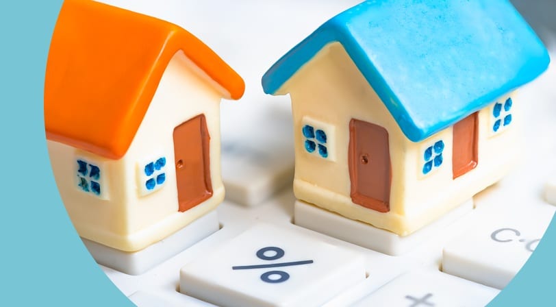 Two small model houses with orange and blue roofs sitting side by side on a calculator keypad near the percent key.