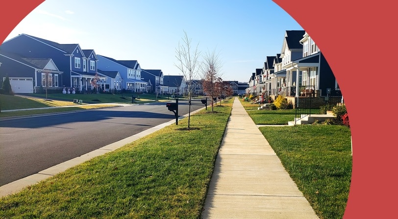 A suburban street lined with two-story homes on both sides and a center sidewalk.