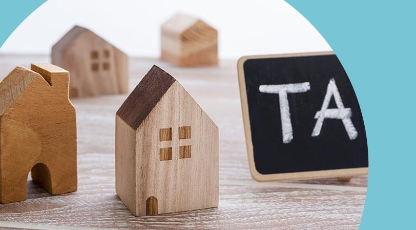 "Tax" written on a whiteboard beside wood house models.