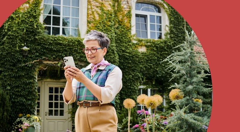 A woman checks her phone in the garden outside an ivy-covered home in a 55+ community.