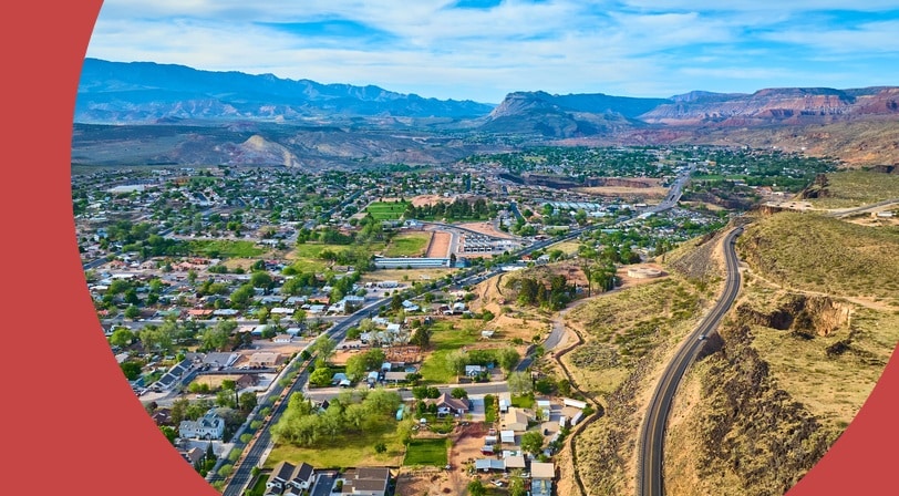 Aerial view of a desert town with tree-lined streets and red rock mountains in the distance.